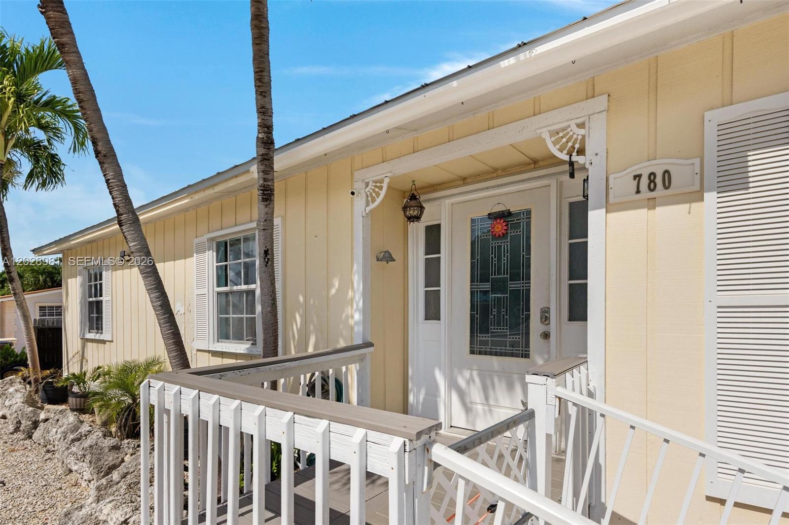 A yellow house exterior features a wooden porch, a white front door, and palm trees — 780 95th Street Ocean, Marathon FL 33050, MARATHON, FL