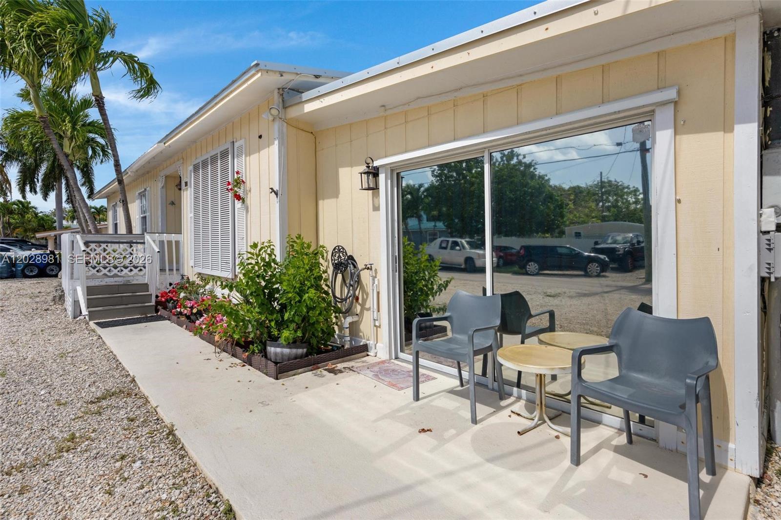 A yellow house exterior features a concrete patio, sliding glass doors, and two gray chairs — 780 95th Street Ocean, Marathon FL 33050, MARATHON, FL
