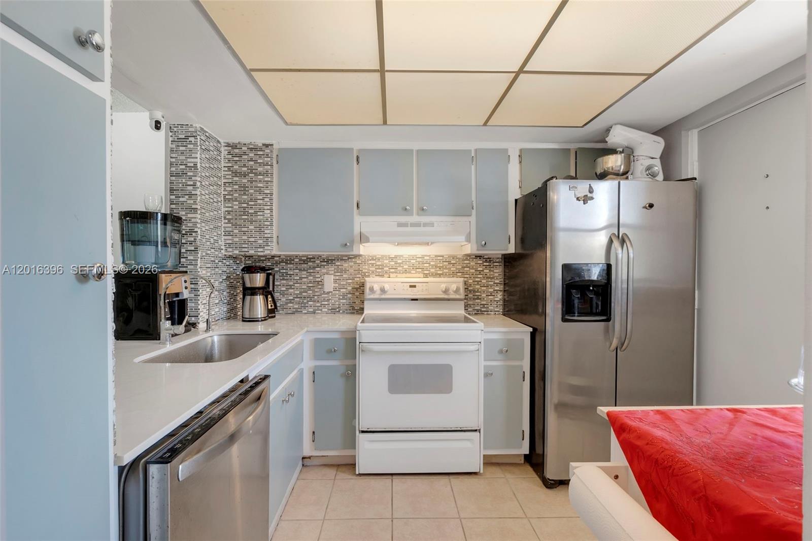 A kitchen features light blue cabinets, stainless steel appliances, a white stove, and tiled flooring — 1101 Crystal Lake Dr # 203, Deerfield Beach FL 33064, DEERFIELD BEACH, FL