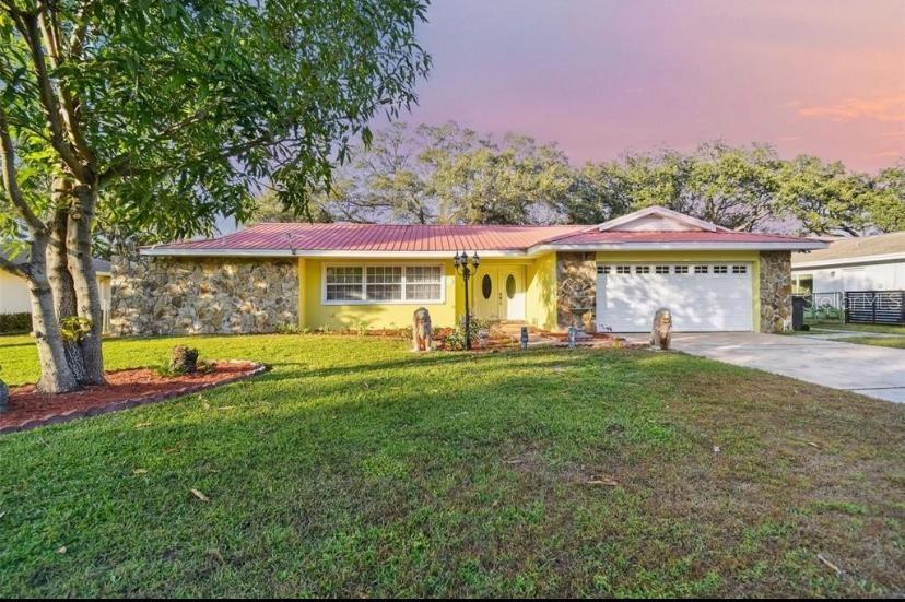 A single-story house with a yellow exterior, stone accents, and a red metal roof — 1514 BURNING TREE LANE, BRANDON, FL
