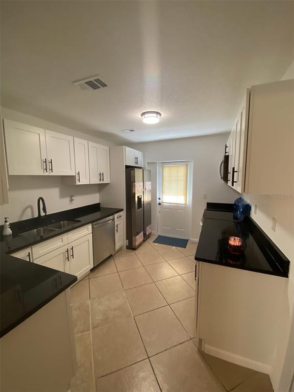 A kitchen features white cabinets, black countertops, stainless steel appliances, and light-colored tile flooring — 1514 BURNING TREE LANE, BRANDON, FL