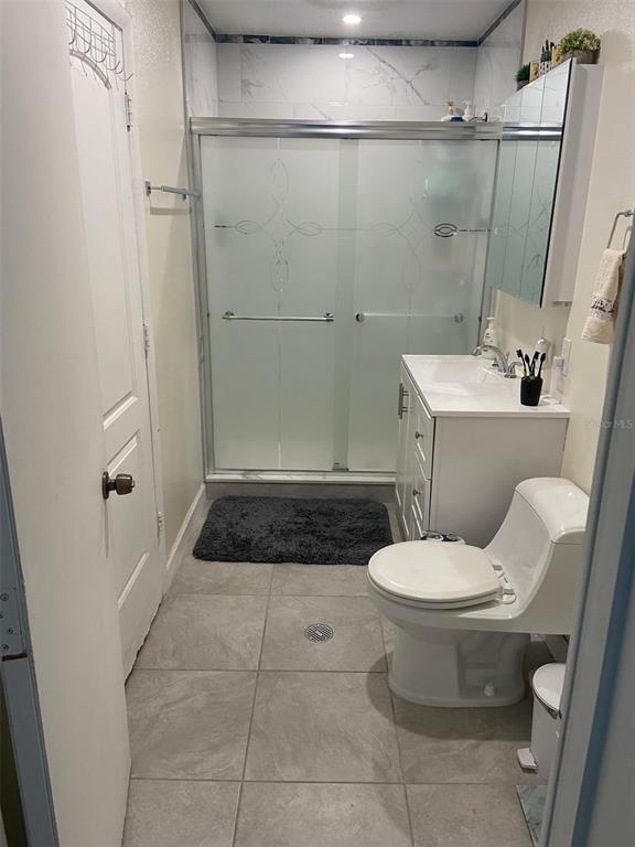 A small bathroom features a walk-in shower, a white vanity, and a toilet on tile flooring — 1514 BURNING TREE LANE, BRANDON, FL