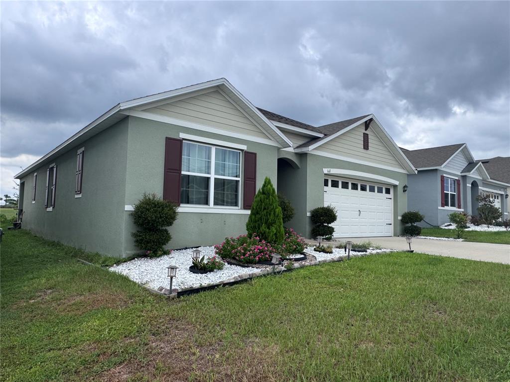 A single-story house with light green stucco, a white garage door, and a white rock garden — 641 GRIFFON AVENUE, LAKE ALFRED, FL