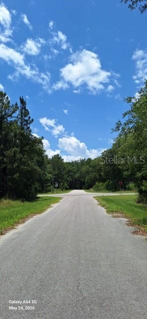 A paved road leads toward a T-intersection surrounded by dense trees under a blue sky — Lot 15 FICHER LANE, OCKLAWAHA, FL