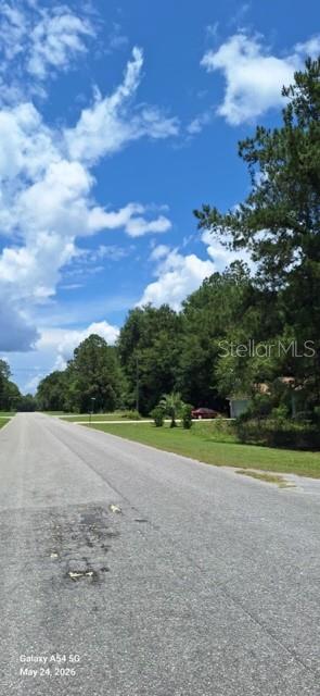 A paved road leads toward a grassy lot bordered by trees under a cloudy sky — Lot 15 FICHER LANE, OCKLAWAHA, FL