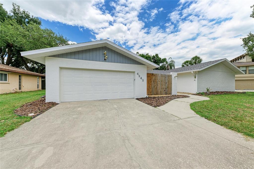 A white house with a two-car garage, a concrete driveway, and a wooden privacy fence — 4242 DRYDEN CIRCLE, SARASOTA, FL