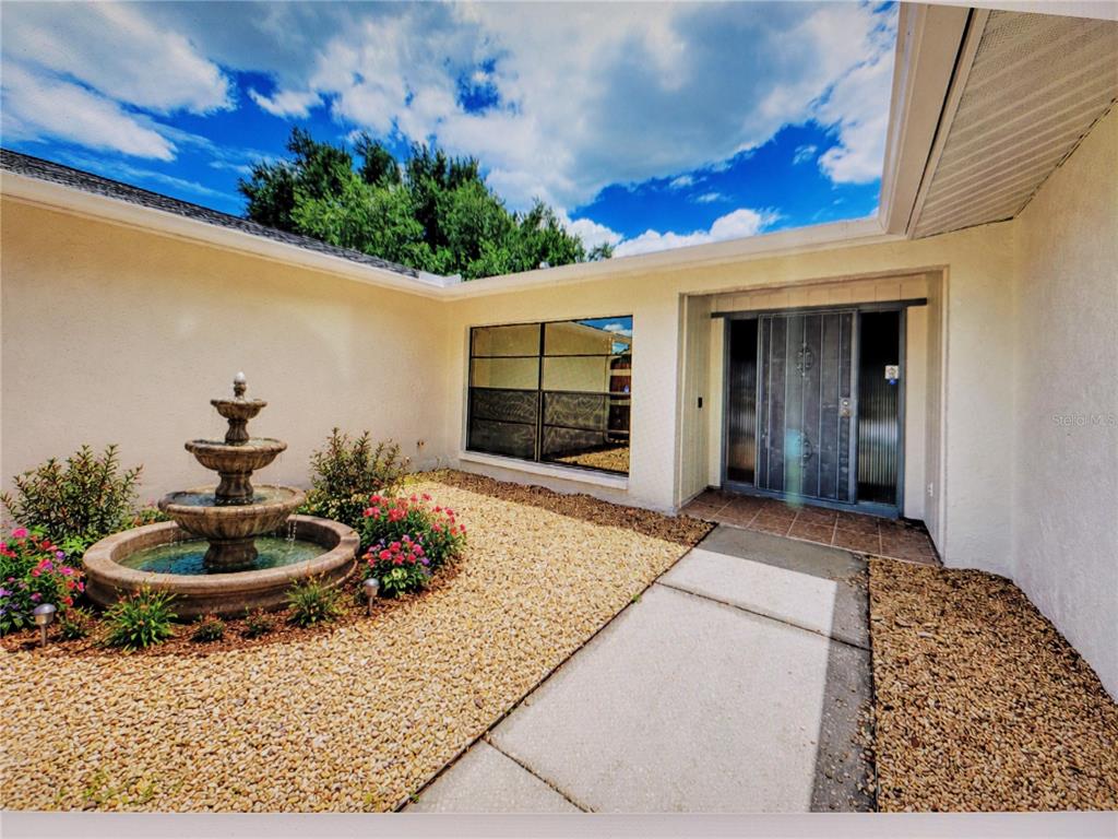 A house exterior features a stone fountain, gravel landscaping, and a metal front door — 4242 DRYDEN CIRCLE, SARASOTA, FL