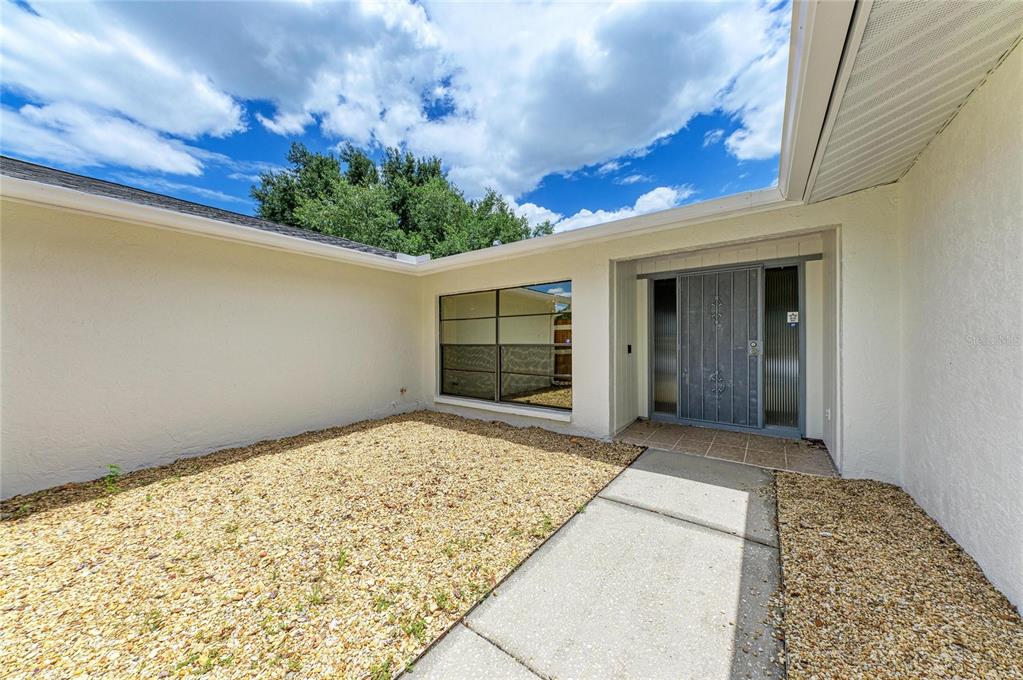 A gravel courtyard leads to the front entrance of a house with a metal door — 4242 DRYDEN CIRCLE, SARASOTA, FL