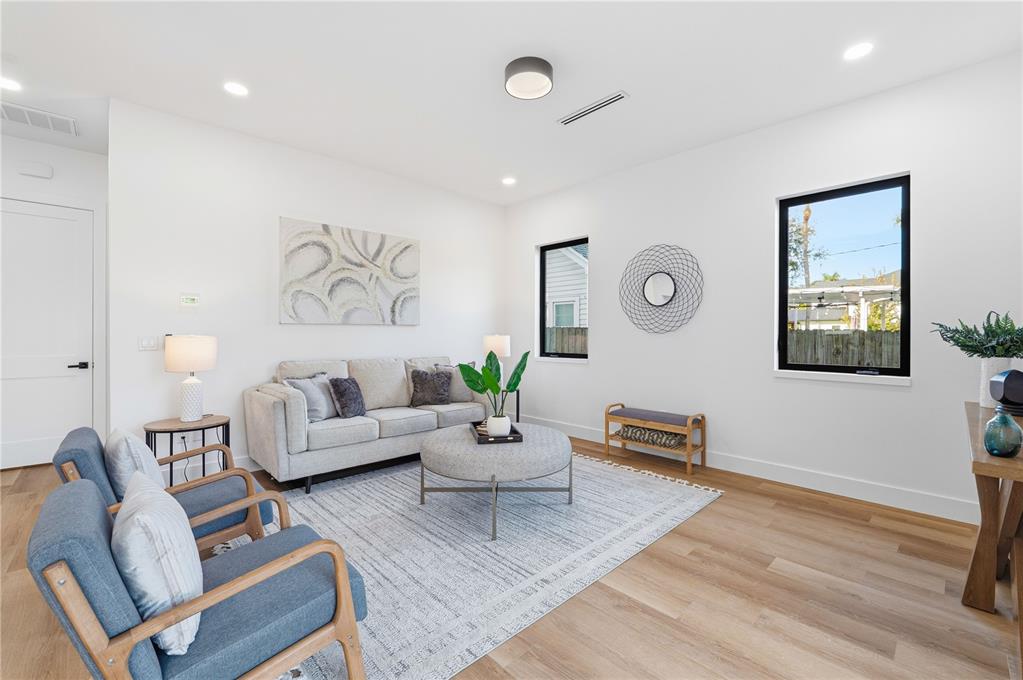 A bright living room features light wood floors, a grey sofa, two blue armchairs, and windows — 3531 81ST STREET N, ST PETERSBURG, FL