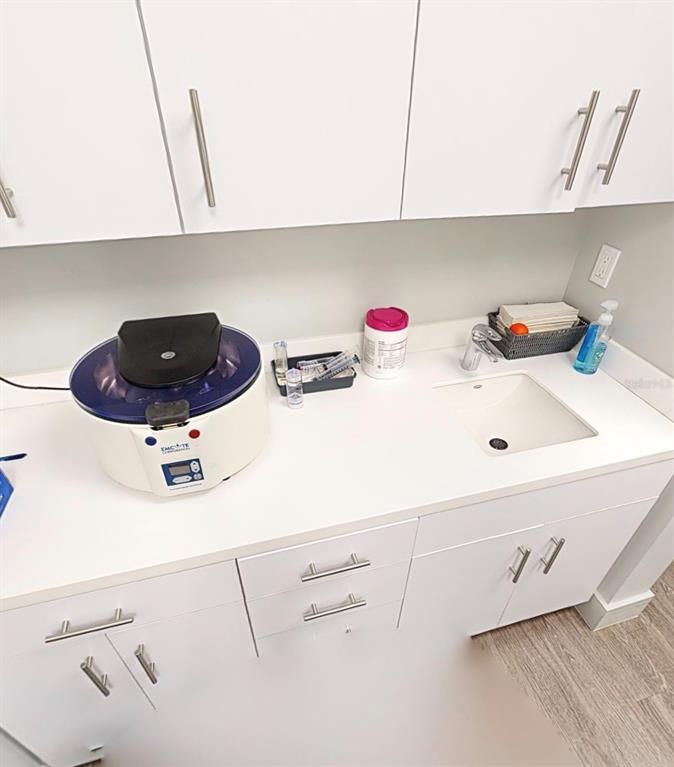 A medical or laboratory room features white cabinets, a countertop, a sink, and a centrifuge — 2555 SW 76TH STREET UNIT 110, GAINESVILLE, FL
