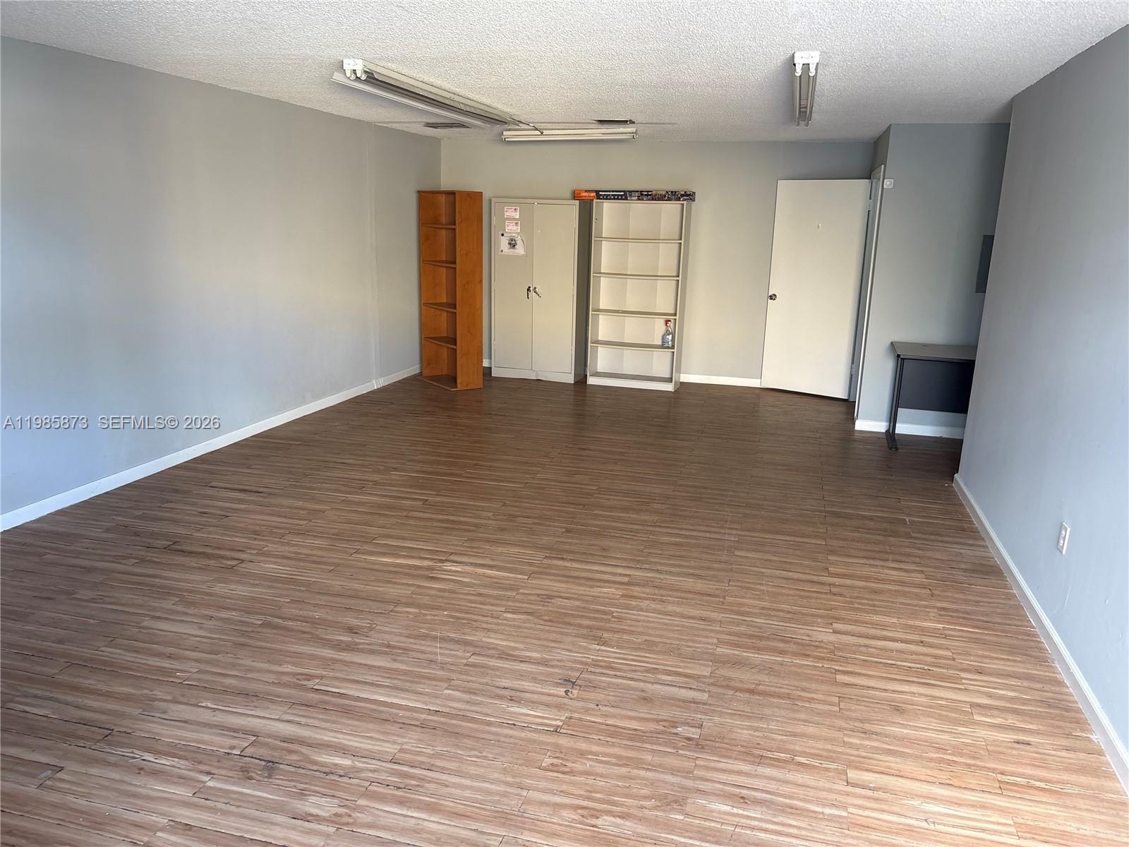An empty room features gray walls, wood-look flooring, fluorescent lighting, and several storage units — 13008 SW 120th St # 5, Miami FL 33186, MIAMI, FL