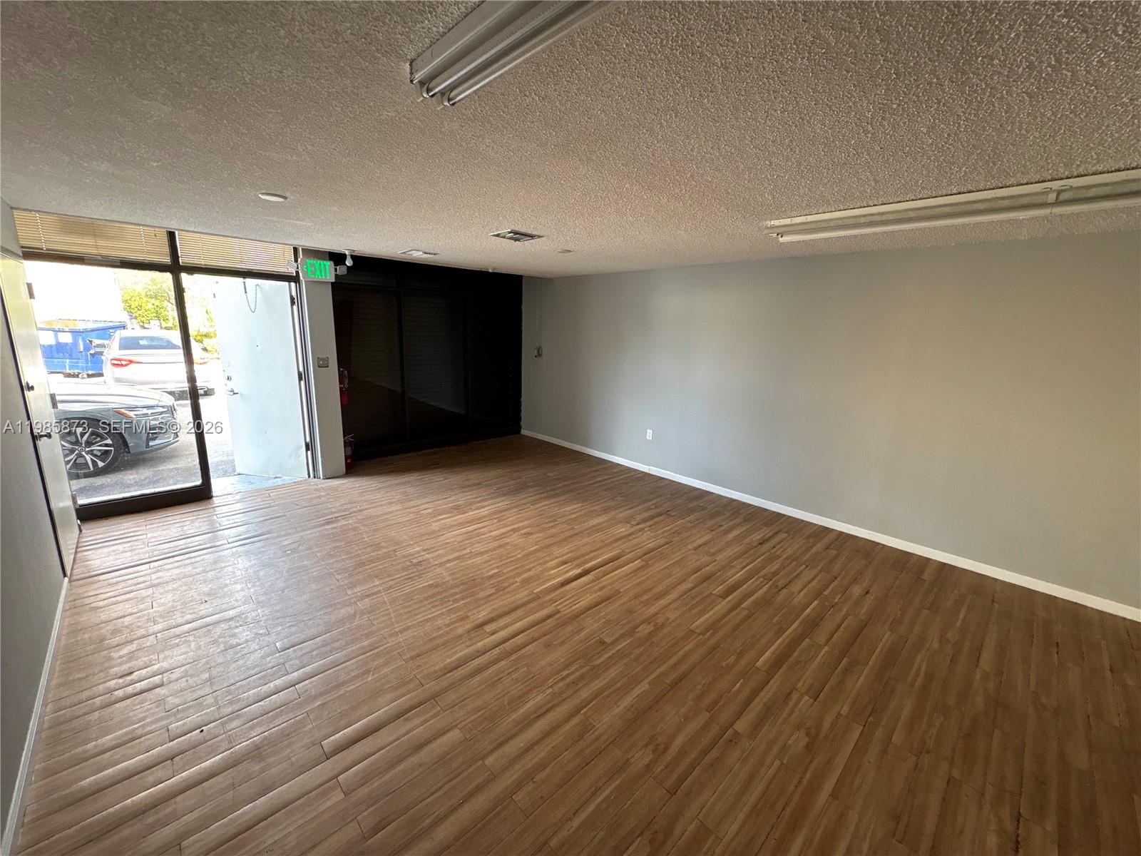 An empty commercial room features wood-look flooring, gray walls, and a glass entrance door — 13008 SW 120th St # 5, Miami FL 33186, MIAMI, FL
