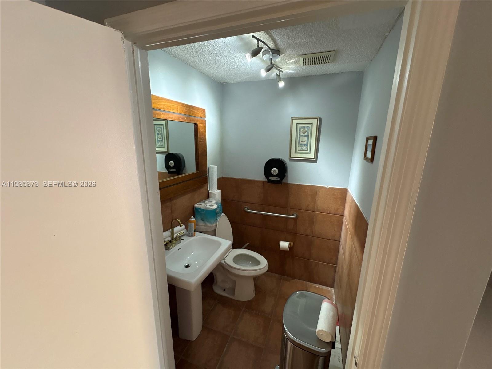 A small bathroom features a pedestal sink, a toilet, and brown tiled walls — 13008 SW 120th St # 5, Miami FL 33186, MIAMI, FL