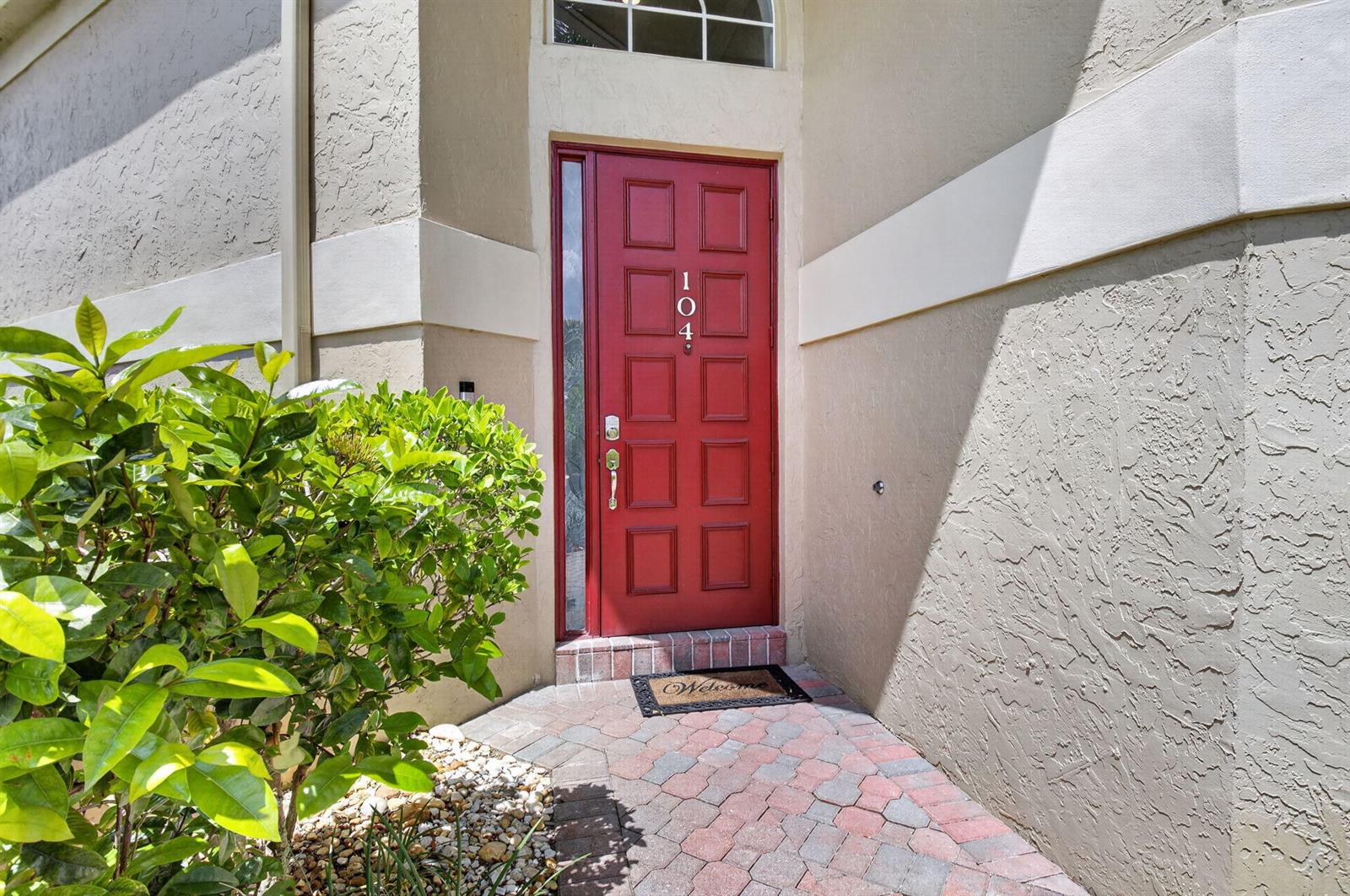 A red front door with a glass sidelight is set in a tan stucco exterior — 17234 Boca Boulevard # 104, Boca Raton FL 33487, BOCA RATON, FL