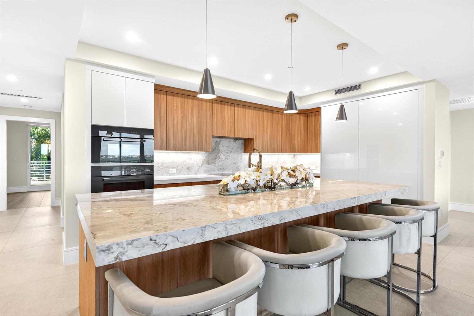 A modern kitchen features a marble island, wood cabinetry, and white high-gloss panels — 1 S Coastal Way # 3030, Jupiter FL 33477, JUPITER, FL