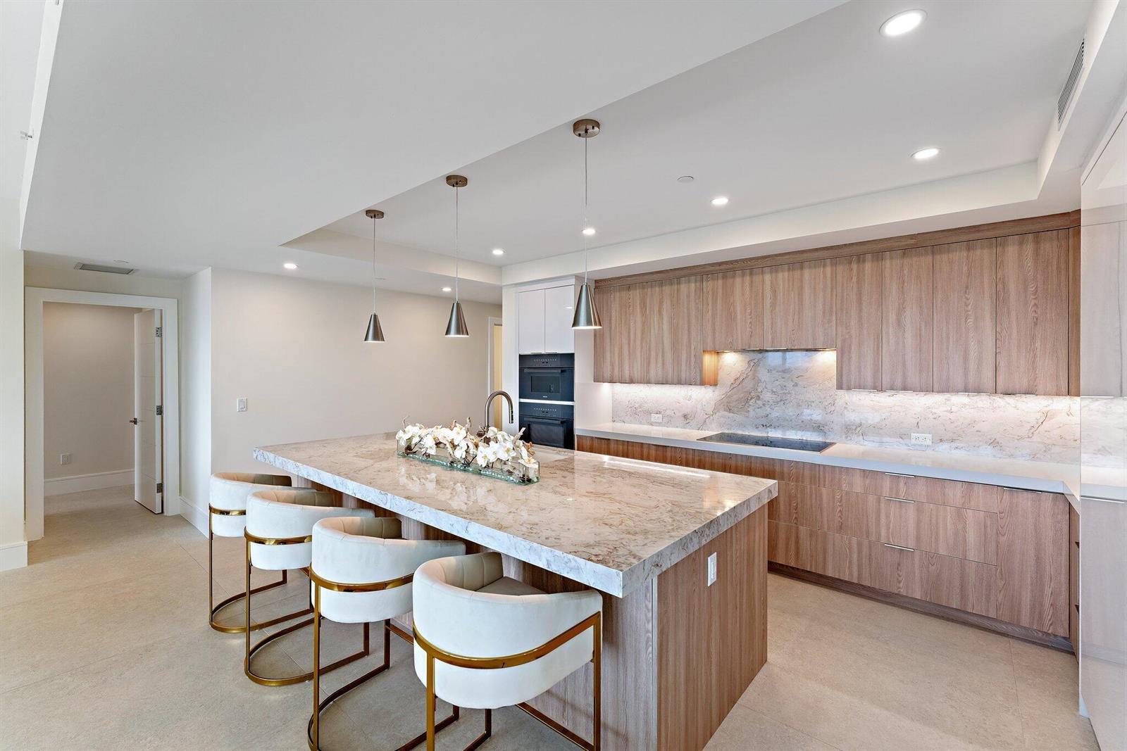 A modern kitchen features a marble island, wood cabinetry, and three pendant lights — 1 S Coastal Way # 3030, Jupiter FL 33477, JUPITER, FL