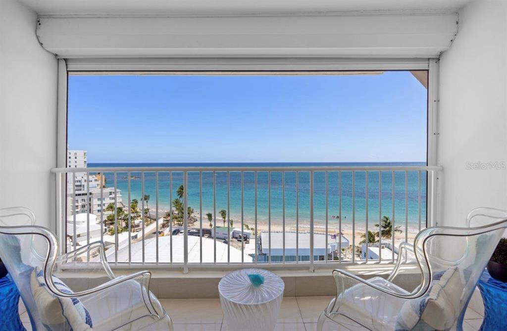 A balcony with two clear chairs and a small table overlooks a beach and ocean — 11 GARDENIA UNIT 1003, CAROLINA, PR