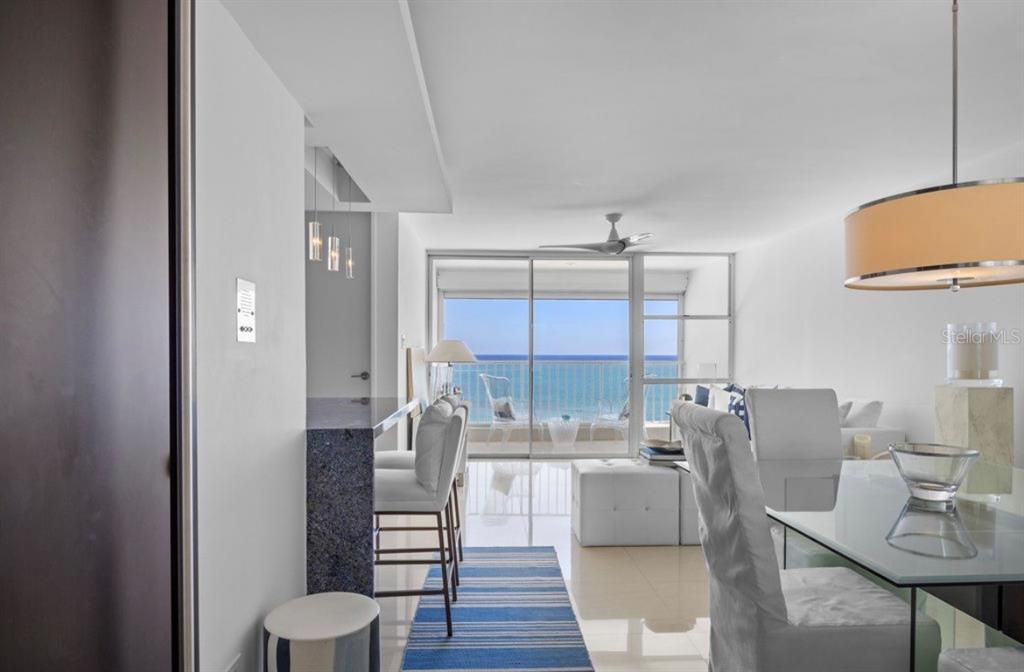 A bright dining and living area features a breakfast bar, white furniture, and ocean views — 11 GARDENIA UNIT 1003, CAROLINA, PR