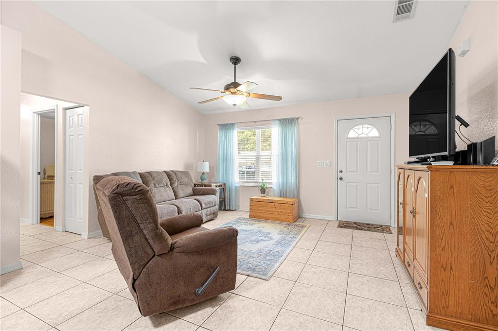 A living room with tile floors, a brown sofa, a recliner, and a television console — 645 SE 56TH AVENUE, OCALA, FL