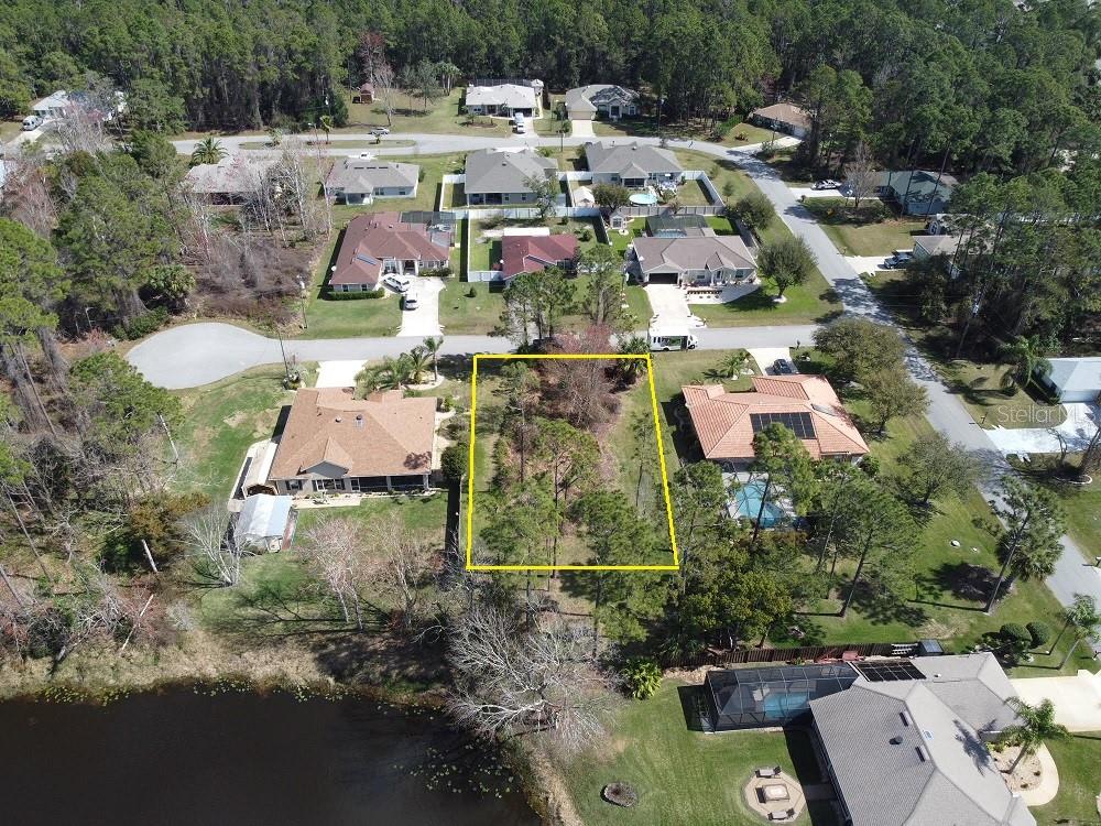 An aerial view shows a vacant, wooded residential lot outlined in yellow between two houses — 3 KALORAMA COURT, PALM COAST, FL