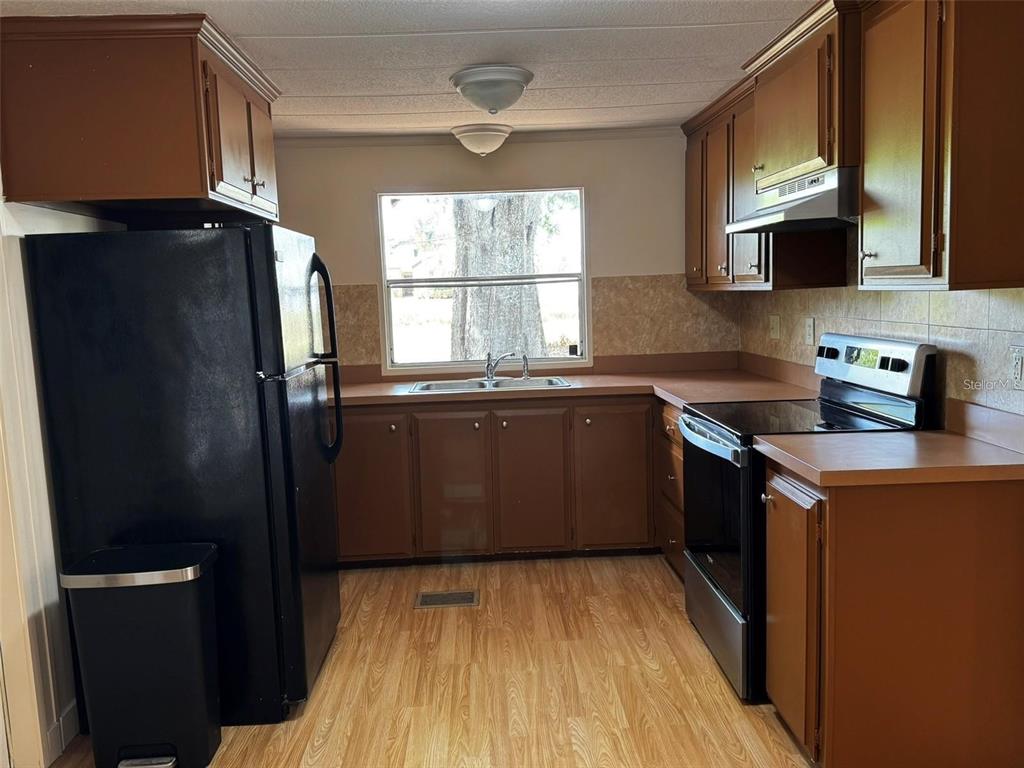 A kitchen features brown cabinets, laminate countertops, a black refrigerator, and a stainless steel stove — 15516 LARKSPUR STREET, ORLANDO, FL