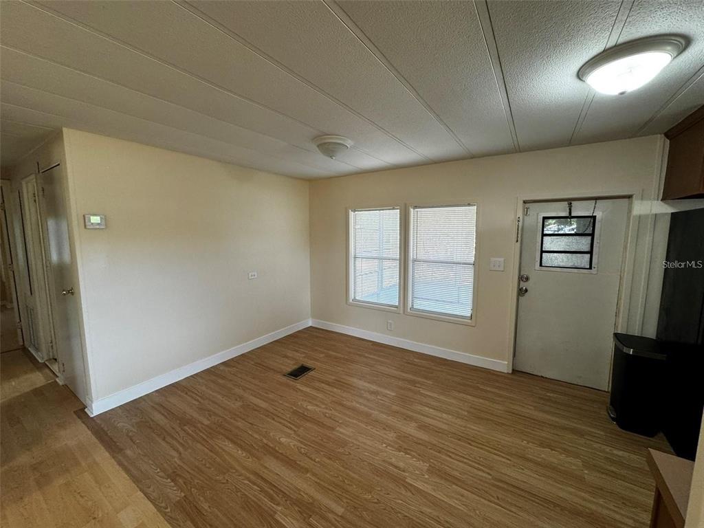 An empty room features light-colored walls, wood-look flooring, two windows, and a white entry door — 15516 LARKSPUR STREET, ORLANDO, FL