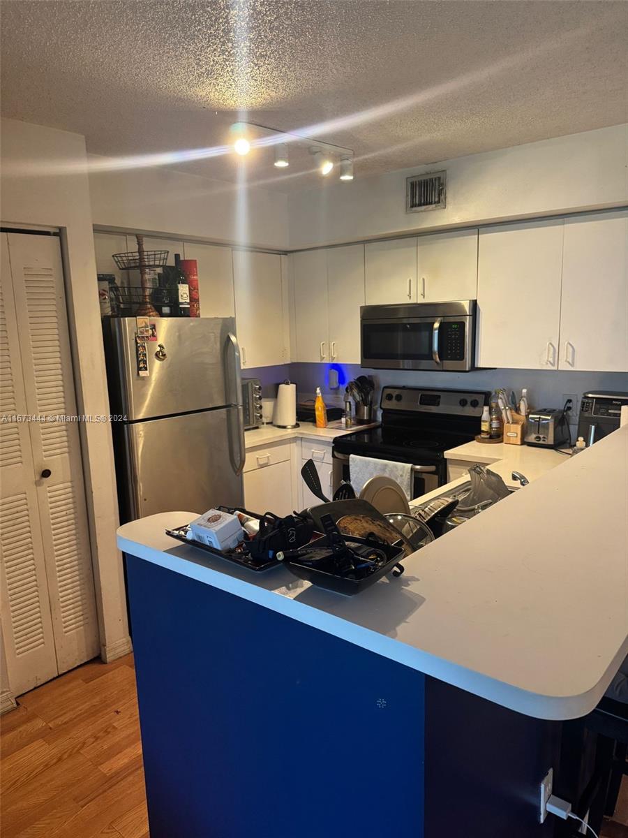 A kitchen features white cabinetry, stainless steel appliances, and a blue-fronted breakfast bar — 4580 NW 107th Ave # 13, Doral FL 33178, DORAL, FL
