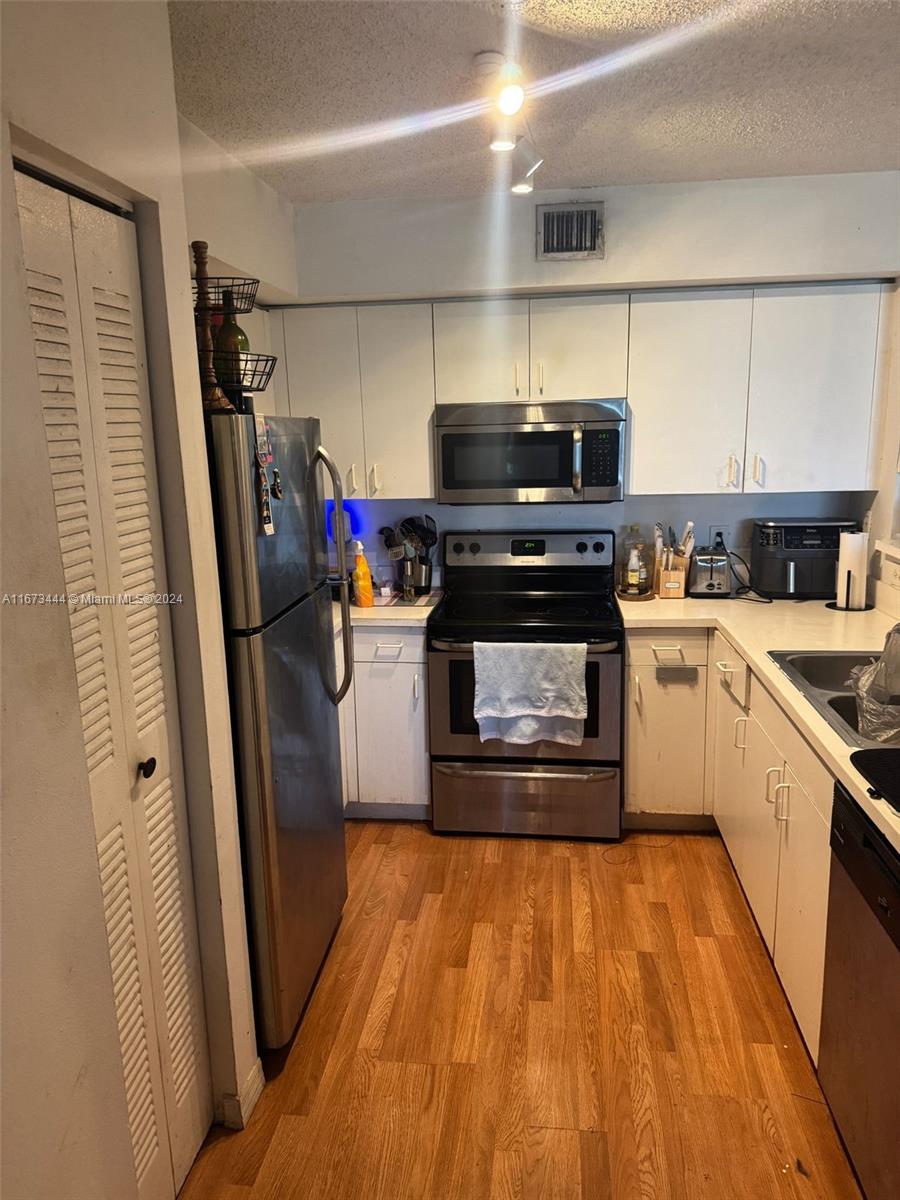 A kitchen with white cabinets, stainless steel appliances, and wood-look flooring — 4580 NW 107th Ave # 13, Doral FL 33178, DORAL, FL