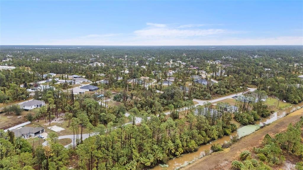 An aerial view shows a residential neighborhood with scattered houses surrounded by dense pine trees — Lot 29 GOURMET ROAD, NORTH PORT, FL
