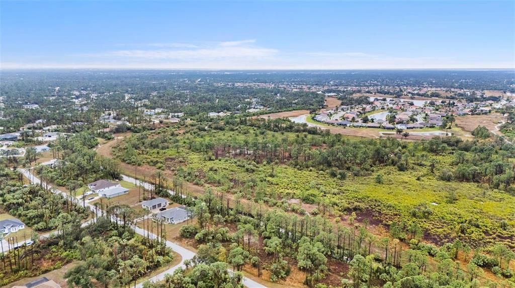 An aerial view shows a residential street with several houses surrounded by dense, undeveloped woodland — Lot 29 GOURMET ROAD, NORTH PORT, FL