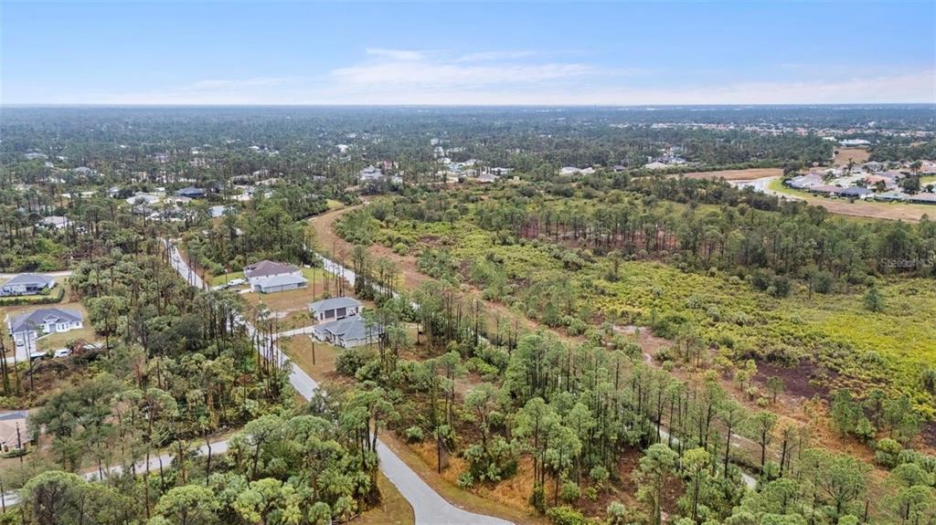 An aerial view shows a residential street with several houses surrounded by dense wooded areas — Lot 29 GOURMET ROAD, NORTH PORT, FL