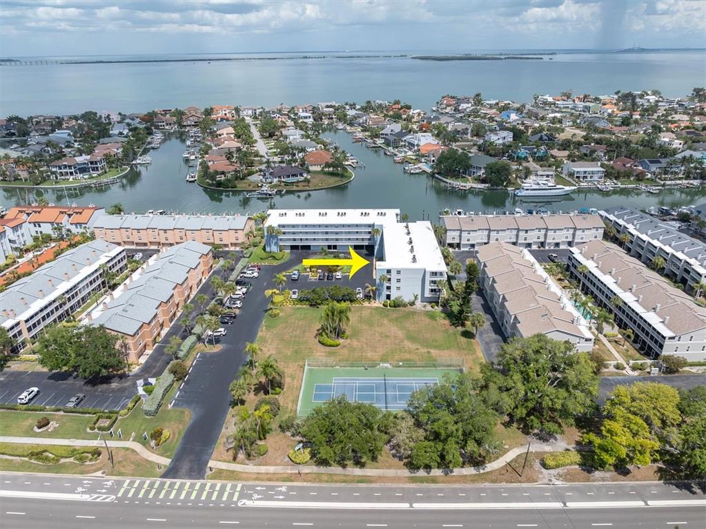 An aerial view shows a multi-story apartment building with a tennis court and parking lot — 719 PINELLAS BAYWAY S UNIT 110, TIERRA VERDE, FL