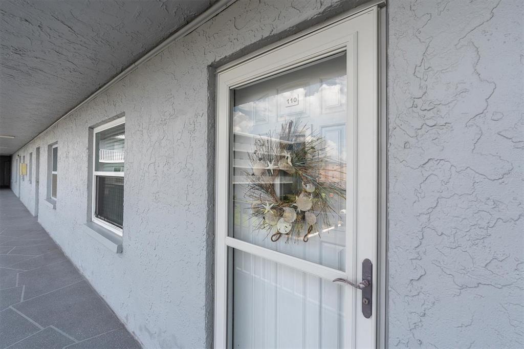 A white storm door with a seashell wreath leads into unit 110 along a walkway — 719 PINELLAS BAYWAY S UNIT 110, TIERRA VERDE, FL