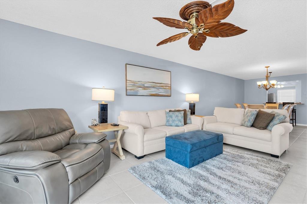 A living room features light blue walls, two beige sofas, a gray recliner, and a fan — 719 PINELLAS BAYWAY S UNIT 110, TIERRA VERDE, FL