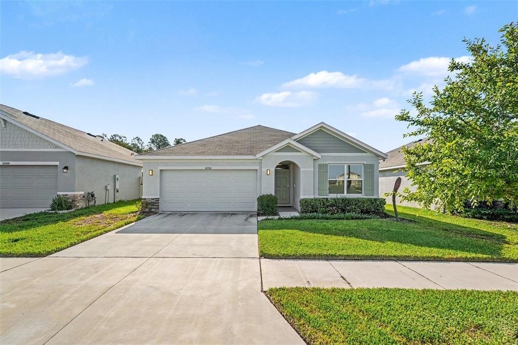 A single-story suburban house with a two-car garage, light siding, and a green lawn — 10792 QUAIL GROVE WAY, SAN ANTONIO, FL