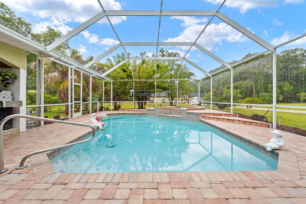 A screened-in swimming pool with a spa and brick paver patio in a backyard setting — 7393 ROYAL OAK DRIVE, SPRING HILL, FL