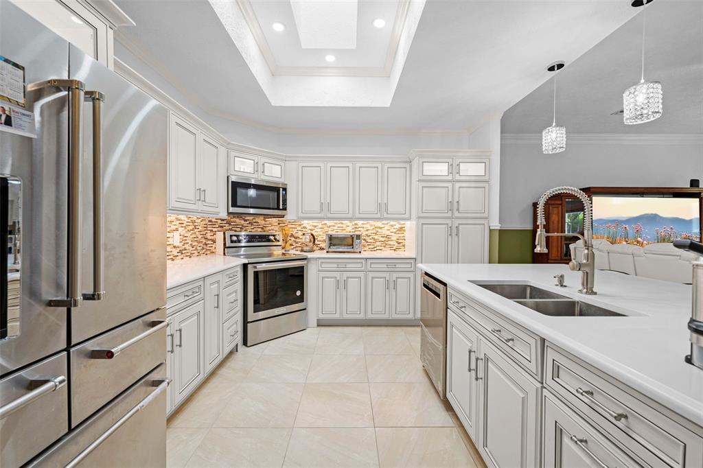 A modern kitchen features white cabinetry, stainless steel appliances, a large island, and tile flooring — 7393 ROYAL OAK DRIVE, SPRING HILL, FL