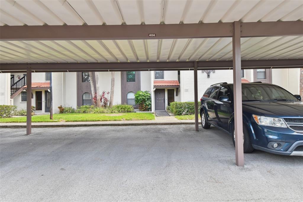A covered parking space sits in front of a multi-story apartment building with landscaping — 3505 TARPON WOODS BOULEVARD UNIT P404, PALM HARBOR, FL