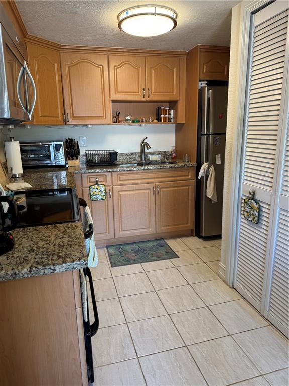 A kitchen features light wood cabinets, granite countertops, stainless steel appliances, and tiled flooring — 3453 CLARK UNIT 252, SARASOTA, FL