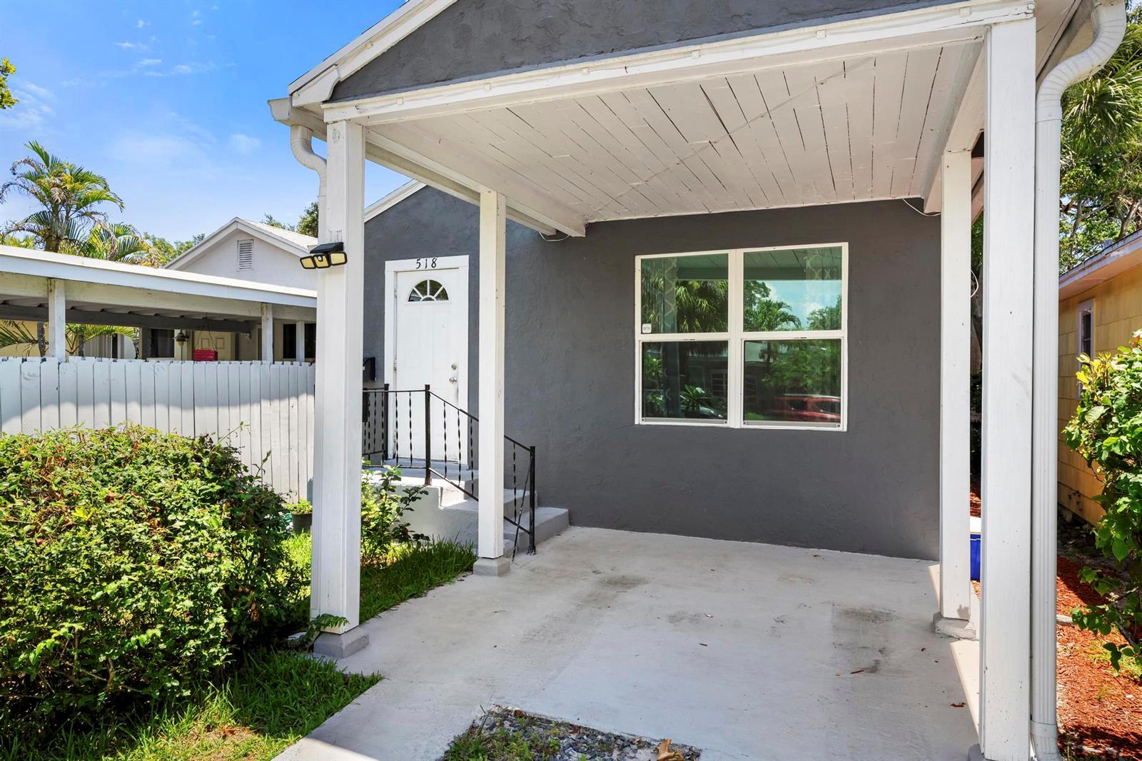 A gray house exterior features a covered concrete carport, a white front door, and windows — 518 N C Street, FL 33460, FL