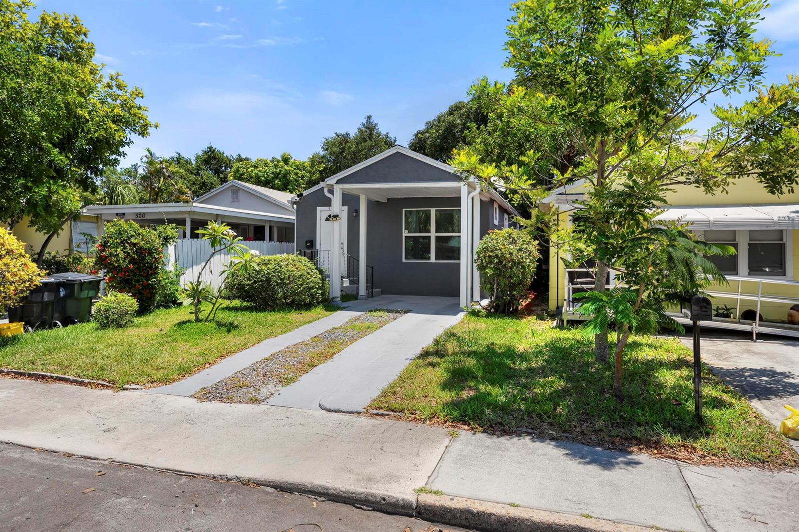 A gray single-story house with a front porch and a concrete driveway sits between two houses — 518 N C Street, FL 33460, FL