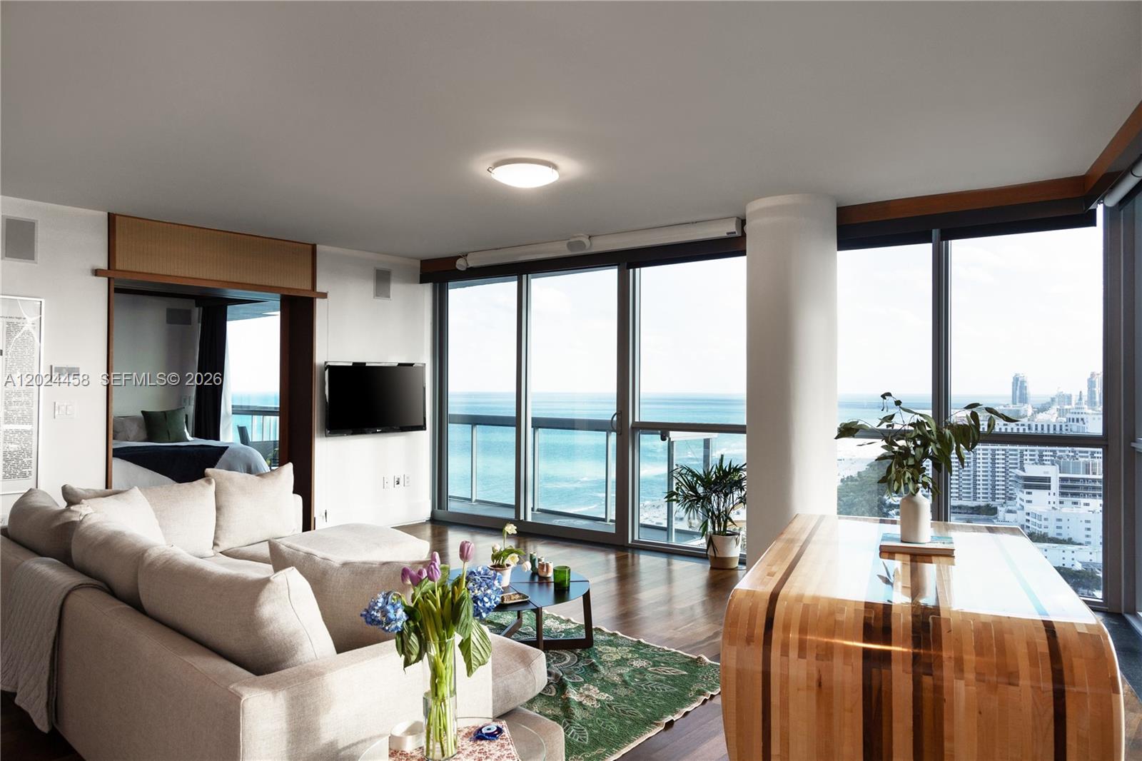 A living room features a sectional sofa, wooden furniture, and floor-to-ceiling windows overlooking the ocean — 101 20th St # 3206, Miami Beach FL 33139, MIAMI BEACH, FL