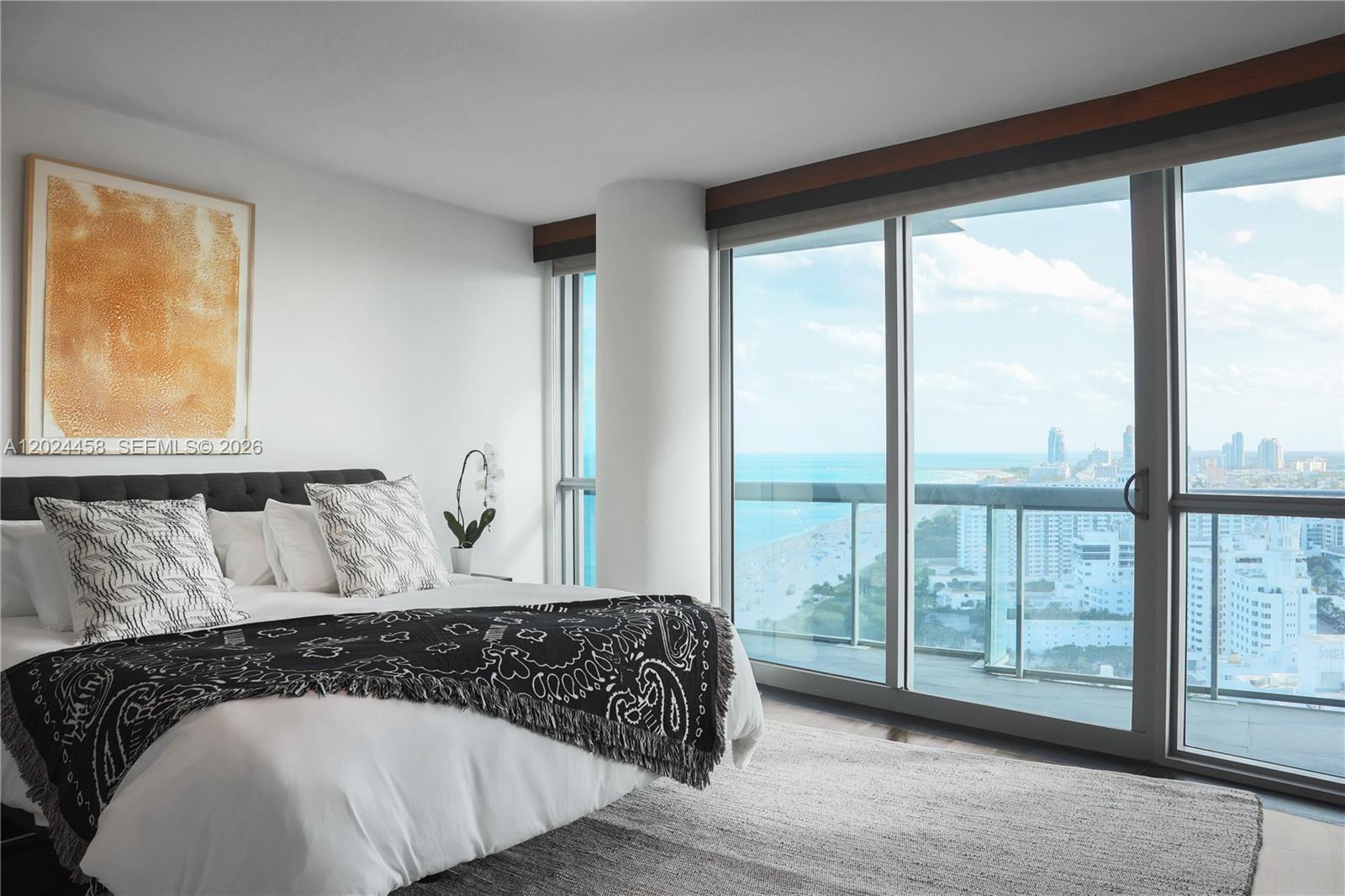 A bedroom features a bed with a patterned throw, white walls, and floor-to-ceiling ocean views — 101 20th St # 3206, Miami Beach FL 33139, MIAMI BEACH, FL