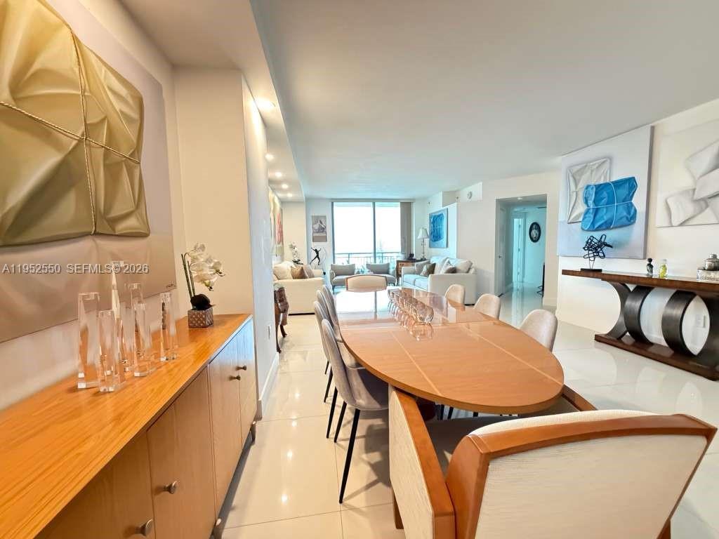 A dining area with a wooden table and sideboard leads into a bright living room — 9066 SW 73rd Ct # 1105, Miami FL 33156, MIAMI, FL