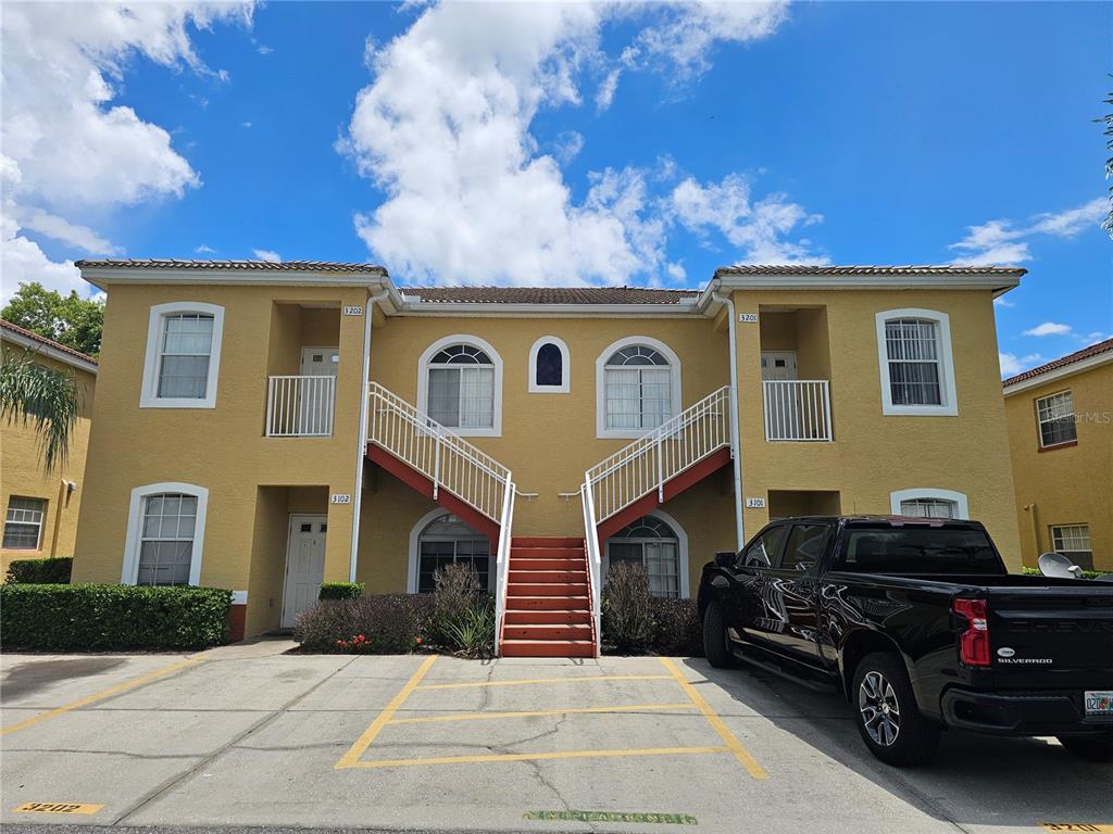 A two-story yellow apartment building with an exterior staircase and a parked black pickup truck — 3201 LAKE MARION RESORT CIRCLE, POINCIANA, FL