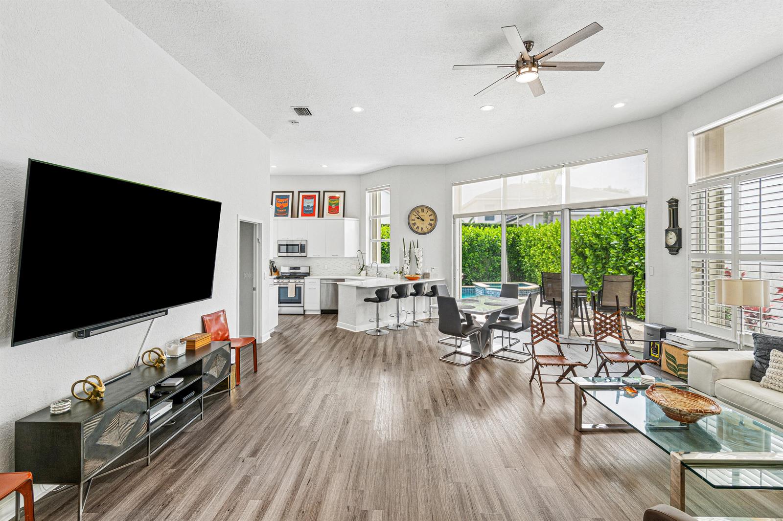 An open-concept living and dining area features wood-look flooring, a large television, and sliding doors — 4278 NW 65th Road, Boca Raton FL 33496, BOCA RATON, FL