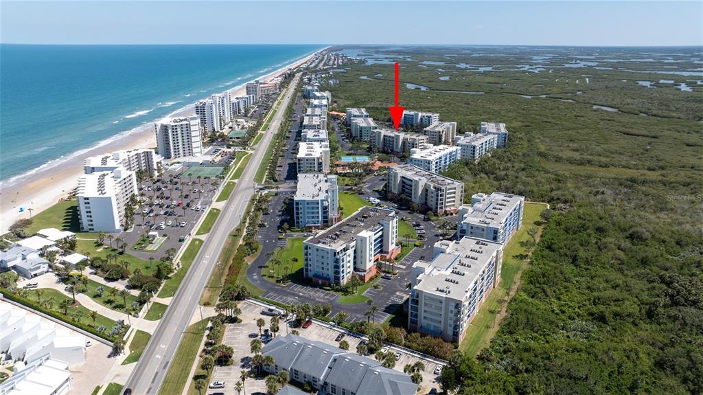 An aerial view shows a coastal condominium complex situated between the ocean and wetlands — 5300 S ATLANTIC AVENUE UNIT 8-304, NEW SMYRNA BEACH, FL
