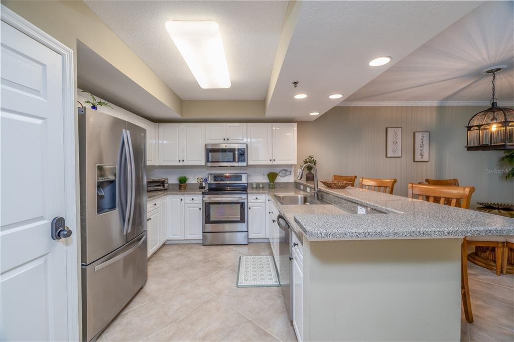 A kitchen with white cabinets, stainless steel appliances, and a granite-topped breakfast bar — 5300 S ATLANTIC AVENUE UNIT 8-304, NEW SMYRNA BEACH, FL