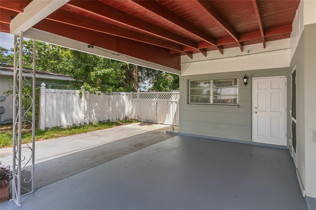A covered concrete carport features a white door, a window, and a white fence — 6518 WALTON WAY, TAMPA, FL