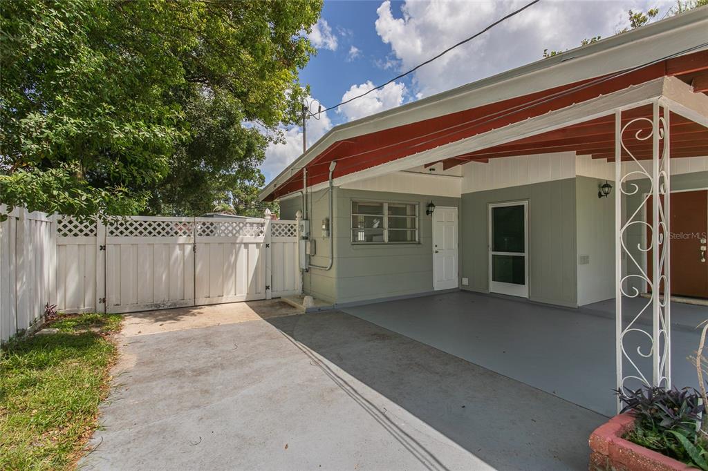 A concrete driveway leads to a covered carport attached to a house with green siding — 6518 WALTON WAY, TAMPA, FL
